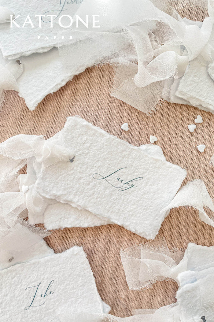 Handmade paper wedding place cards with deckled edges, personalized calligraphy names, romantic fine art table styling.