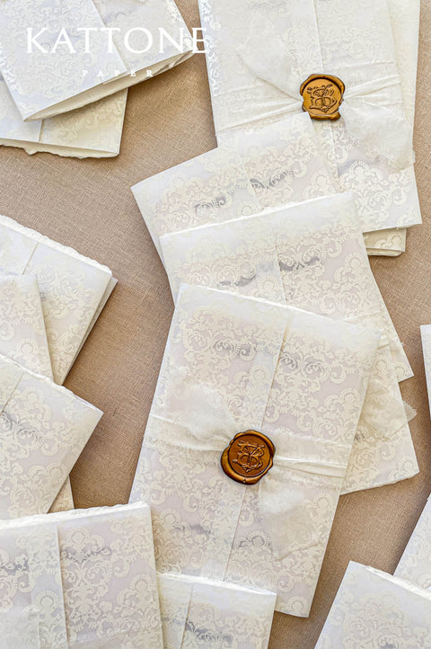 Luxury wedding invitation with patterned envelope liner, ivory envelope, silk ribbon wrap, and gold wax seal monogram.