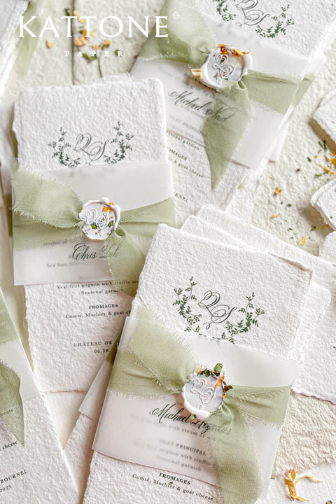 These handmade paper wedding menus are the epitome of timeless elegance and refined craftsmanship. Made from 100% cotton rag paper, each piece features a beautifully textured surface and natural deckled edges, exuding the charm of fine art stationery. The menu design showcases a botanical-inspired monogram delicately printed in deep green ink, creating a harmonious blend of organic beauty and understated luxury.