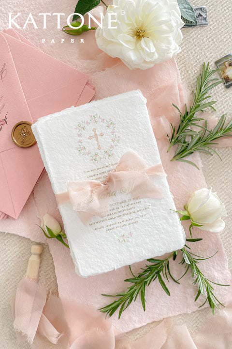 A soft and elegant christening invitation crafted from luxurious handmade paper and finished with a blush chiffon ribbon. Featuring a delicate watercolor floral wreath and subtle Christian cross, this design beautifully celebrates faith, innocence, and new beginnings. Perfect for baptisms, christenings, and church ceremonies, it creates a heartfelt keepsake your family will treasure.