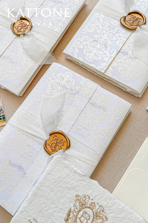 Close-up of handmade cotton paper wedding invitation with natural deckled edges, soft paper texture, elegant gold typography.