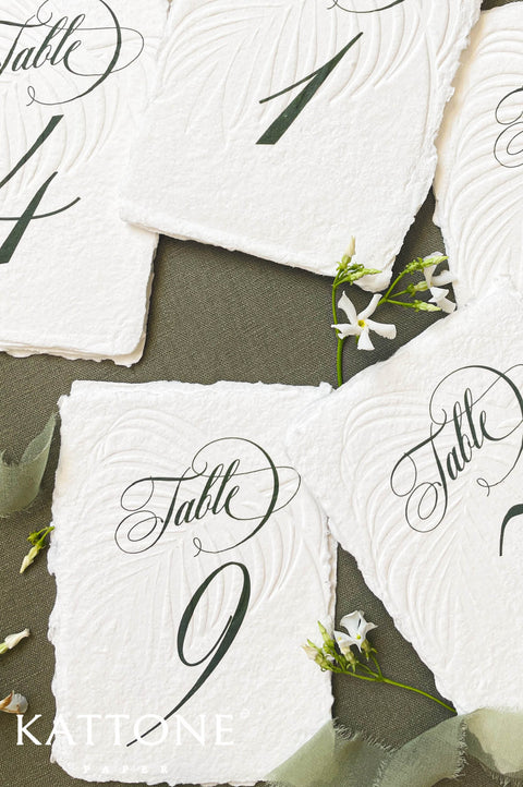 Assorted handmade paper table numbers featuring elegant script and organic torn edges.