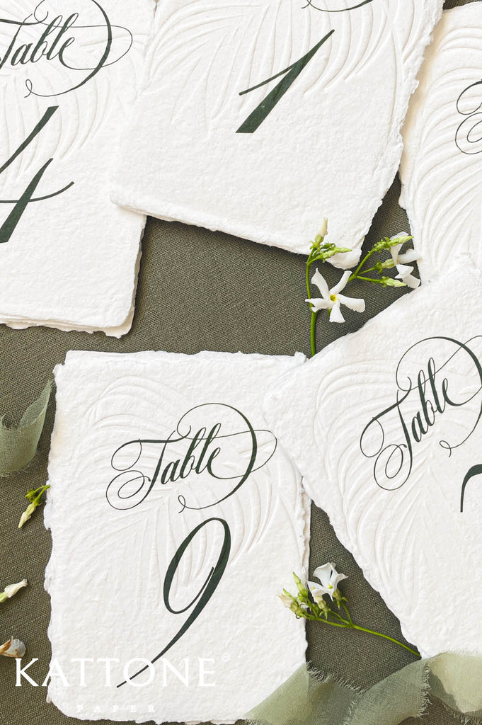Assorted handmade paper table numbers featuring elegant script and organic torn edges.