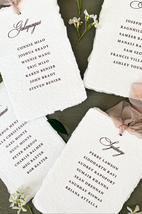 Assorted handmade paper place cards styled with ribbon and florals for a wedding table.
