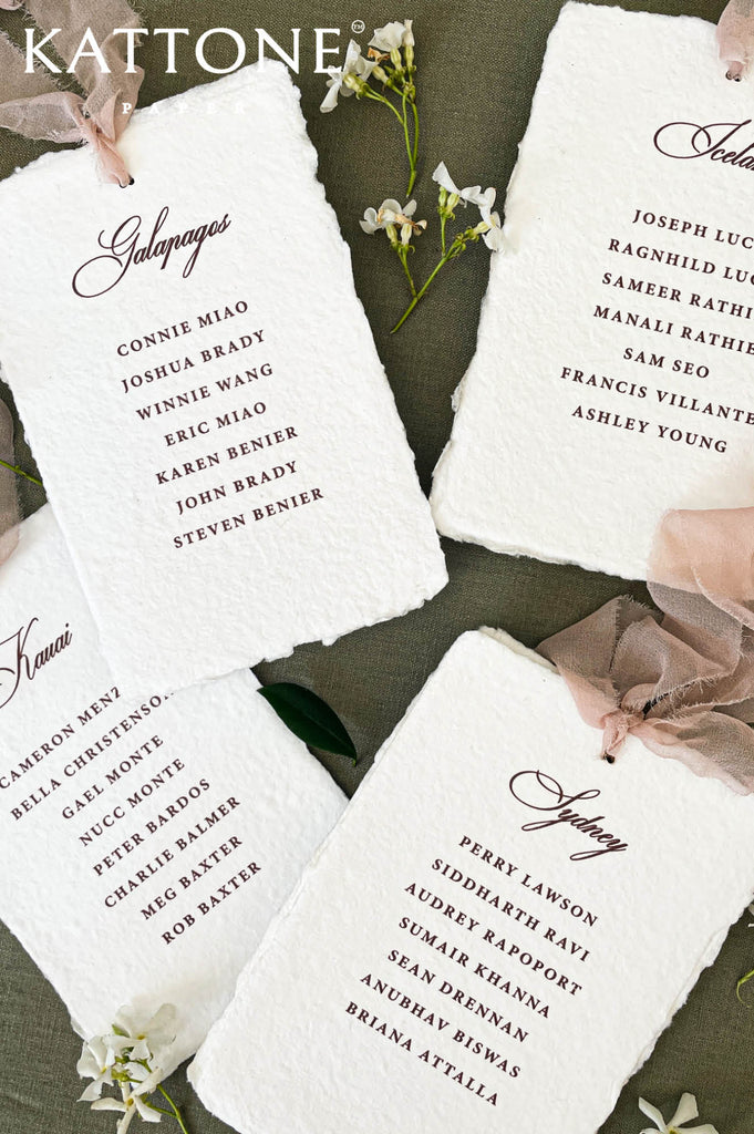 Assorted handmade paper place cards styled with ribbon and florals for a wedding table.