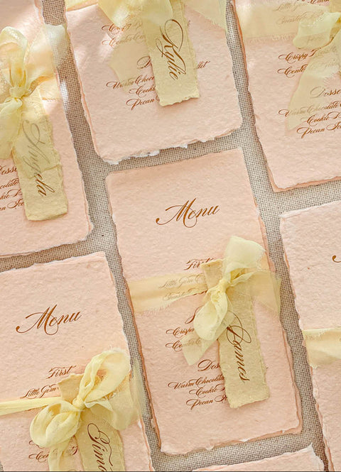 Bring warmth and romantic elegance to your tables with our colored handmade paper menus, crafted on premium cotton paper with softly deckled edges. Each piece features beautiful script typography, custom name tags, and silk-chiffon ribbons that add delicate texture and charm. Perfect for spring, garden, or fine-art weddings, these menus blend artisanal craftsmanship with graceful color palettes to complete your reception styling.