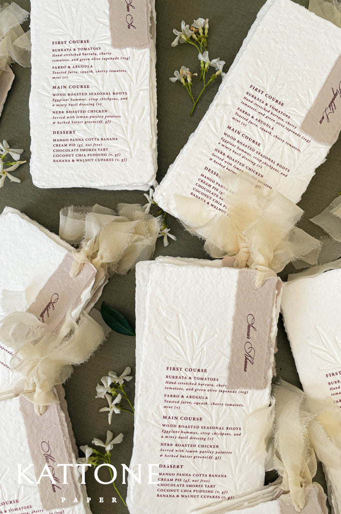 Flat lay of luxury wedding table stationery featuring handmade paper menus styled with ribbon and florals.