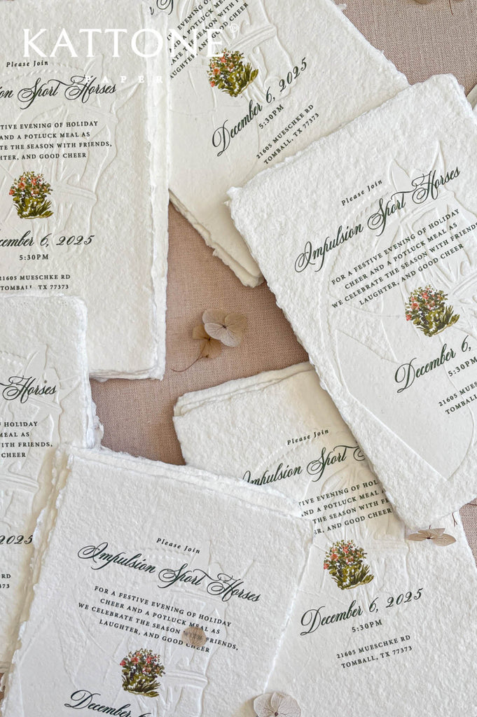 Close-up of embossed handmade paper wedding invitation showing watercolor artwork, textured cotton paper, and fine embossing.