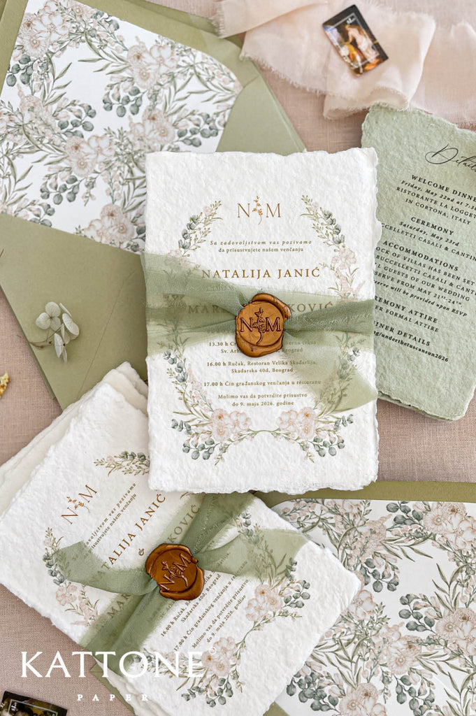 Sage green silk ribbon wrapped around handmade wedding invitation secured with warm-toned wax seal featuring monogram initials.