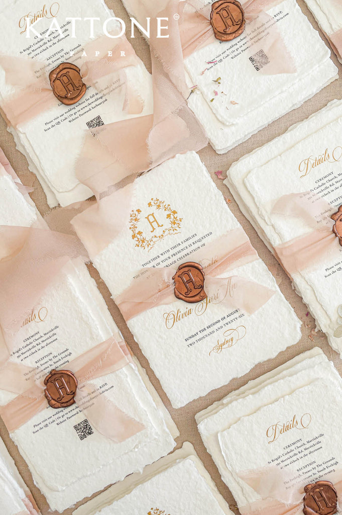 Flat lay of luxury wedding stationery suite with handmade paper invitations, details cards, monogram crest, and blush silk ribbon styling.
