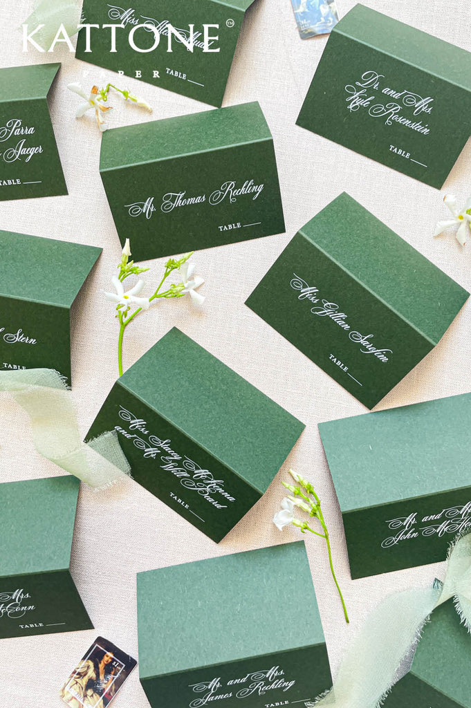 Assorted green tent-style wedding place cards displayed on a neutral linen background.