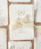 Close-up flat lay of a handmade paper wedding thank you card with deckled edges, soft gold typography, and a delicate floral crest, styled on neutral linen