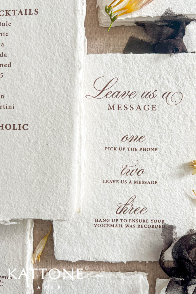 A close-up of a rustic white paper menu card with torn edges, printed with elegant script and serif text including 'Leave us a MESSAGE' and numbered options one through three. The card is styled on a neutral surface with dried yellow flowers and dark ribbon accents.