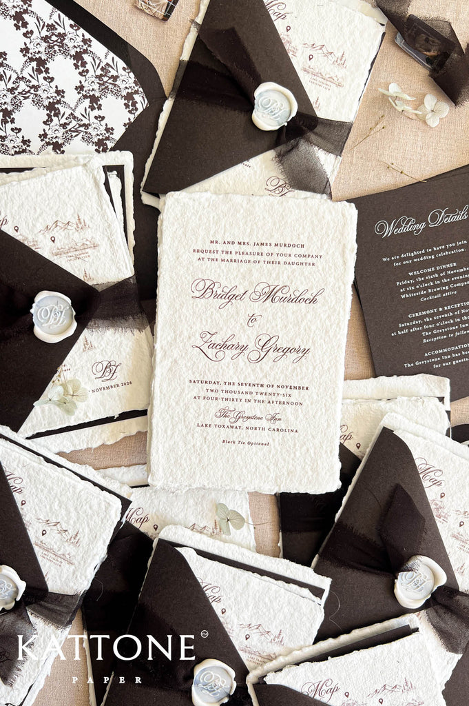 A styled flat-lay of wedding stationery featuring a central textured off-white invitation surrounded by coordinating black envelopes, cream paper inserts, ribbon ties, and wax seals on a tan background. The brand name 'KATTONE PAPER' appears in the lower-left corner.