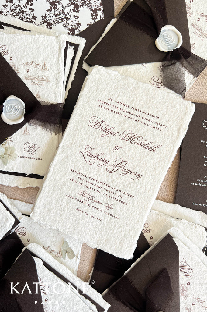 A styled flat-lay of wedding stationery featuring a textured off-white invitation card with elegant cursive text, paired with dark brown envelopes, black ribbons, and white wax seals.
