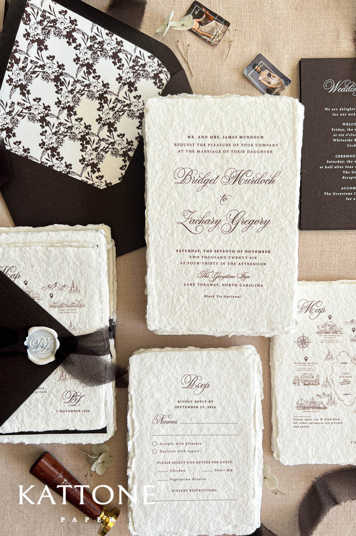 Top-down flat lay of luxury brown wedding invitation suite featuring ivory handmade deckled-edge paper, chocolate brown envelopes, floral patterned envelope liner, custom wedding map card, RSVP card, dark details card, sheer dark ribbon, and personalized white wax seal