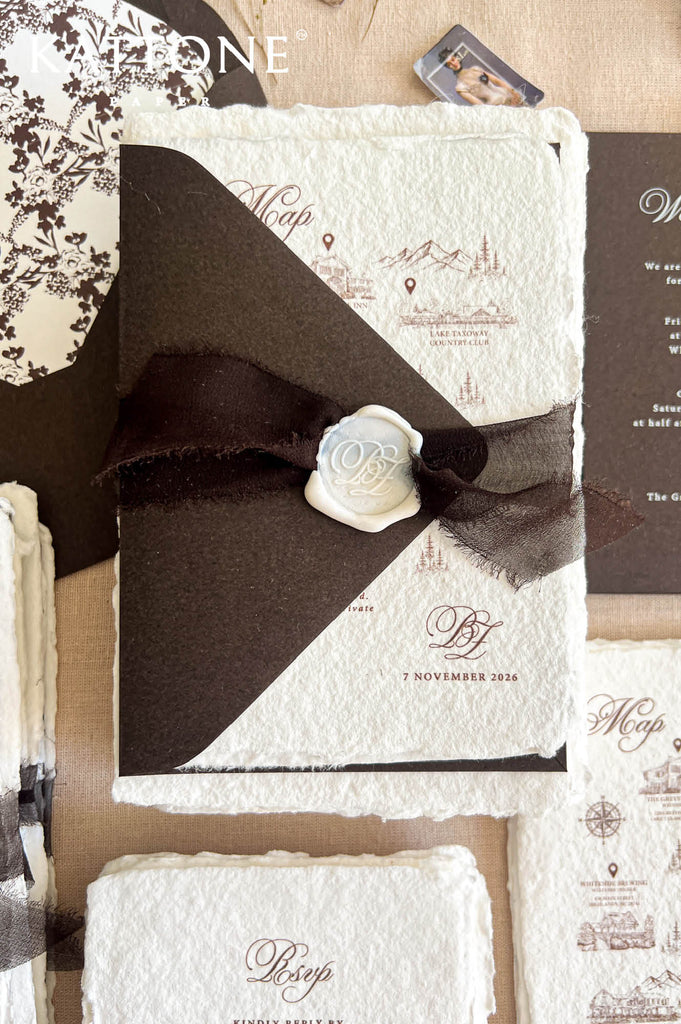 A styled flat-lay of a vintage-inspired wedding invitation suite. The main piece is a square invitation card featuring a textured off-white paper background with a dark brown diagonal band, a dark brown ribbon, and a white wax seal with a monogram 'OB'.