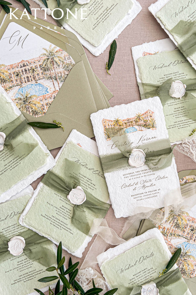 Overhead flat lay of personalized sage green wedding envelopes with watercolor resort liners, soft olive tones, monogram details, and surrounding handmade wedding stationery styled on neutral linen