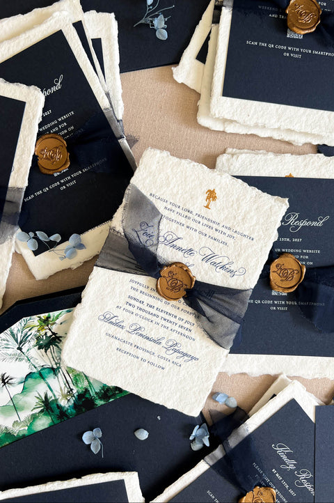 A styled flat-lay of wedding stationery from Kattone Paper, featuring textured cream and navy cards, ribbons, wax seals, and botanical prints on a neutral beige background.