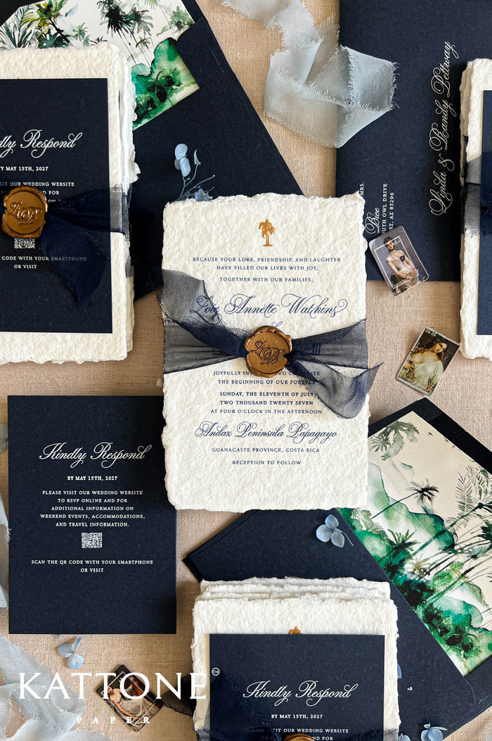A styled flat-lay of wedding stationery from Kattonal, featuring navy blue and cream textured paper invitations, envelopes, a wax seal, botanical prints, and small photo cards arranged on a neutral background.