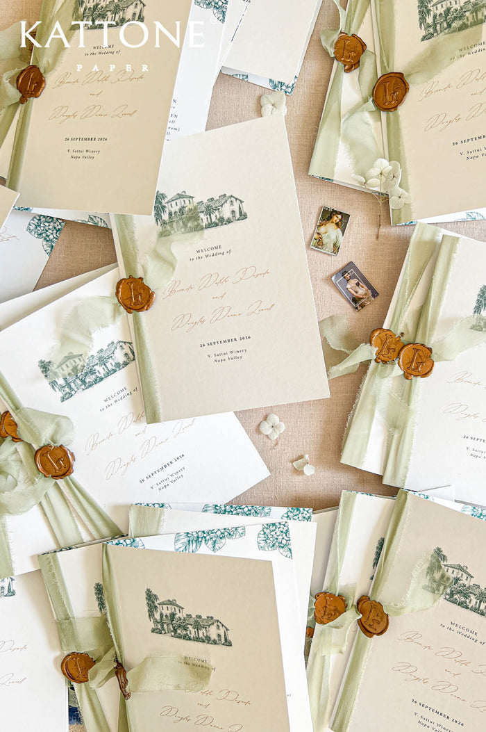 Top-down close-up of two folded wedding programs opened side by side, featuring soft green botanical border artwork, elegant script headings, and black ceremony text, styled with sage green ribbon and neutral wedding stationery on a linen background
