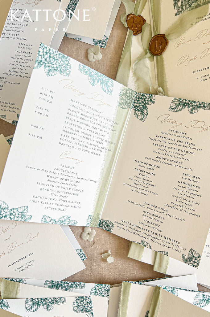 Overhead close-up of opened folded wedding programs showing ceremony timeline and wedding party details, with green botanical border illustrations, refined typography, and coordinating stationery layered on a linen backdrop
