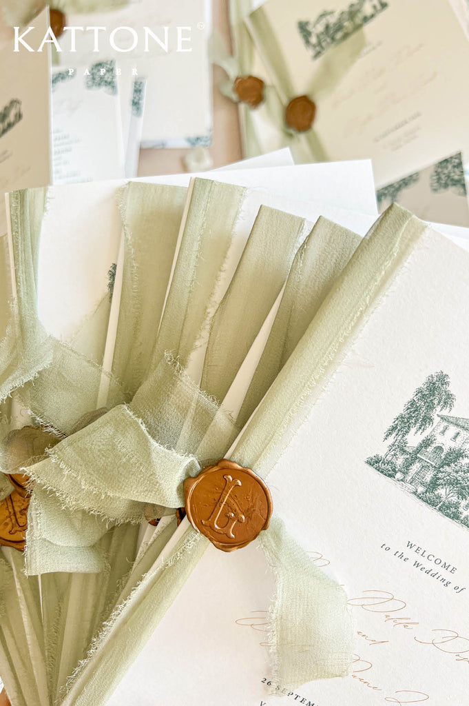 A close-up of wedding stationery featuring cream-colored cards with green architectural illustrations, tied with pale sage green ribbon and sealed with brown wax. The brand name KATTONE STATIONERY is visible in the top left corner.