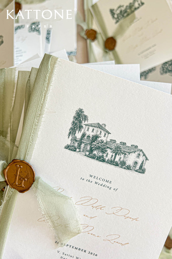 A close-up of wedding stationery featuring a cream-colored textured invitation card with a dark green architectural illustration and elegant script text, tied with a pale green ribbon and a round brown wax seal. Additional matching cards and envelopes are softly blurred in the background.