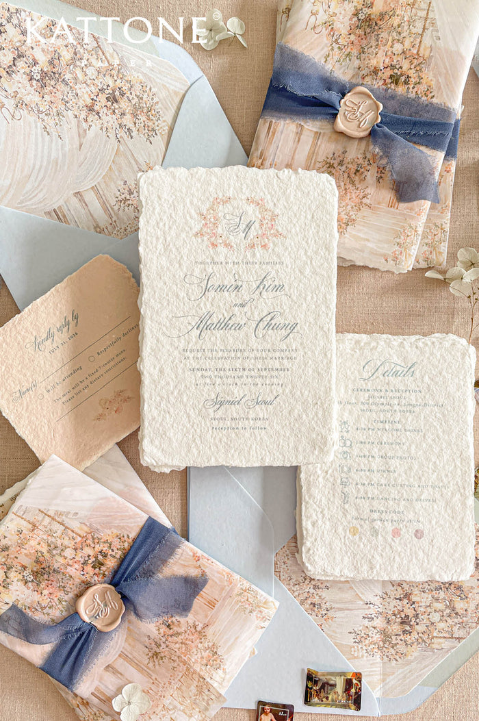 A styled flat-lay of a wedding invitation suite from Kattone, featuring textured cream paper, floral watercolor designs, dusty blue ribbons, and gold wax seals on a neutral beige background.