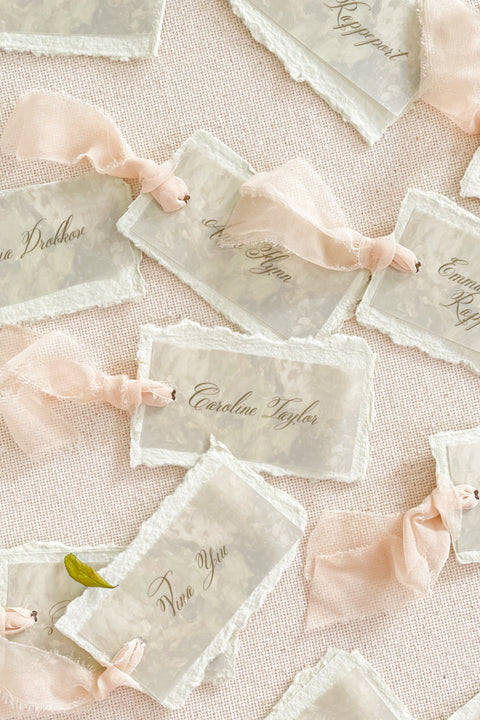 Add ethereal elegance to your event with our handmade paper place cards, crafted from delicate cotton rag paper and layered with a translucent vellum top sheet. Each card is finished with naturally torn deckled edges and soft blush ribbon, creating a dreamy fine-art look perfect for weddings, showers, and romantic celebrations. These unique layered cards bring texture, movement, and refined beauty to every tablescape.