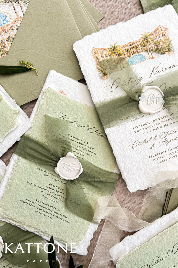 Overhead styled flat lay of handmade paper wedding invitations with watercolor resort artwork, sage green details cards, olive envelopes, soft green ribbon, personalized wax seals, botanical greenery, and tropical destination wedding stationery