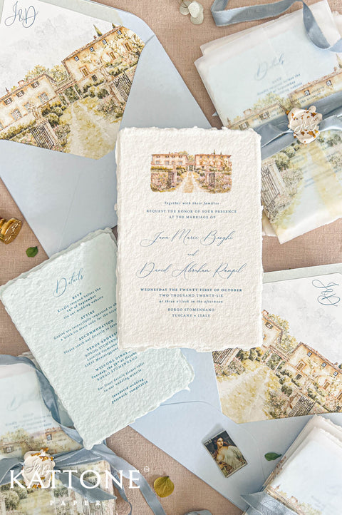 A styled flat-lay of wedding invitation suite stationery from Kattone Invitations, featuring textured cream and pale blue cards, matching envelopes, ribbons, and printed villa illustrations on a neutral beige background.
