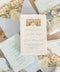 Top-down flat lay of luxury Tuscany wedding invitation suite featuring handmade deckled-edge paper, pale blue envelopes with watercolor Borgo Stomennano venue liners, translucent vellum jackets, dusty blue silk ribbon, personalized wax seals, and elegant Italian destination wedding stationery