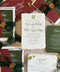 Top-down flat lay of luxury burgundy and forest green wedding invitation suite featuring ivory handmade deckled-edge paper, elegant calligraphy, burgundy envelopes, green details cards, dark sheer ribbon, antique-gold monogram wax seals, and coordinating RSVP stationery