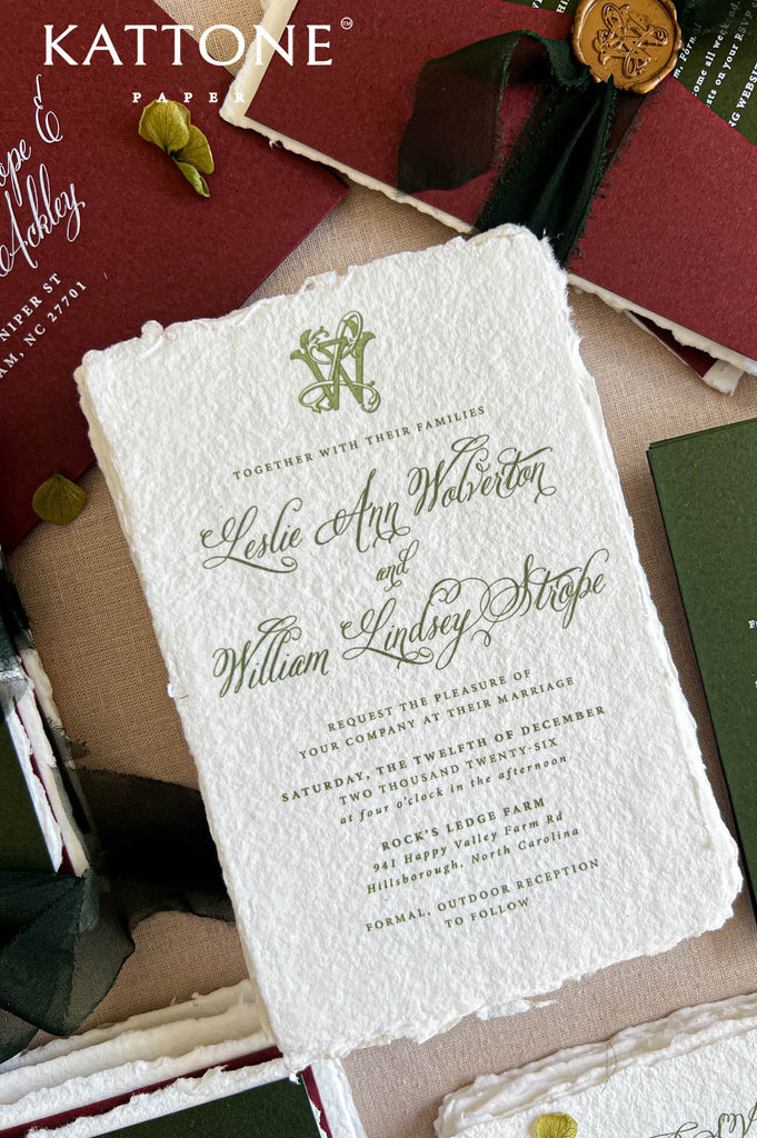 A styled flat-lay of a wedding invitation card on textured off-white paper, surrounded by matching stationery including a burgundy envelope with a gold seal, a dark green card, and a Kattone Paper logo at the top left.