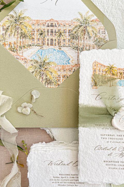 Close-up overhead view of handmade deckled-edge wedding invitation with watercolor tropical resort artwork, sage green silk ribbon, ivory monogram wax seal, and coordinating pale green weekend details card on neutral linen