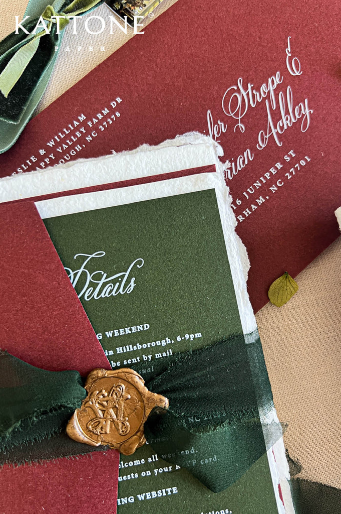 A styled flat-lay of a wedding invitation suite featuring a deep burgundy envelope, a dark green watercolor details card with white script text, a dark green ribbon, and a gold wax seal with an embossed horse and rider.
