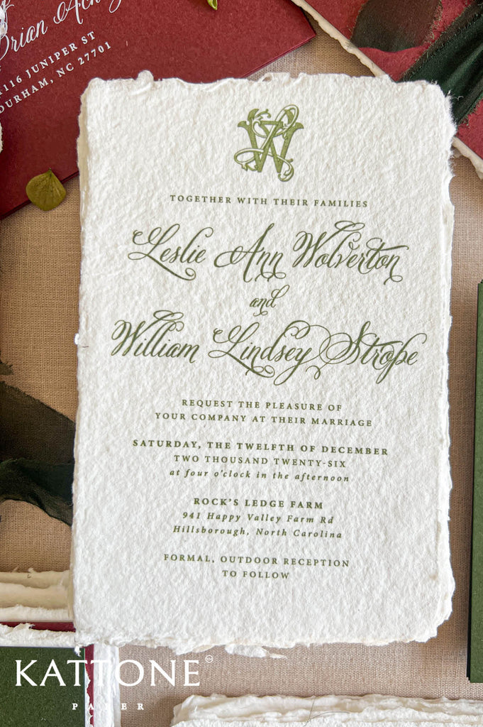 A square wedding invitation card with textured off-white paper and elegant green script text, photographed flat on a neutral surface with decorative props around the edges. The Kattone Paper logo appears in the bottom-left corner.