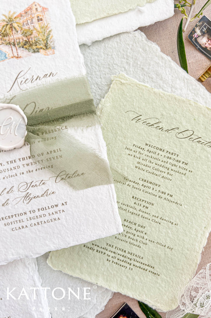 Angled close-up of pale sage green handmade paper weekend details card with deckled edges and elegant script typography, layered beside ivory wedding invitation, soft green ribbon, personalized wax seal, and botanical styling