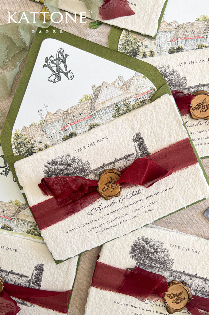 Angled overhead close-up of luxury handmade paper save the date card wrapped with burgundy ribbon and personalized bronze wax seal, layered over an olive green envelope with custom watercolor venue liner and monogram artwork