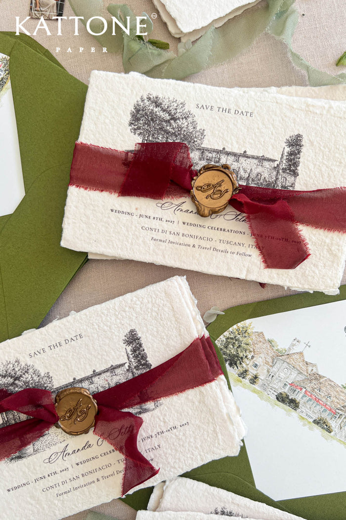 Top-down flat lay of handmade deckled-edge save the date cards featuring black architectural venue illustrations, deep burgundy sheer ribbon, bronze monogram wax seals, olive green envelopes, and watercolor envelope liners styled on neutral linen