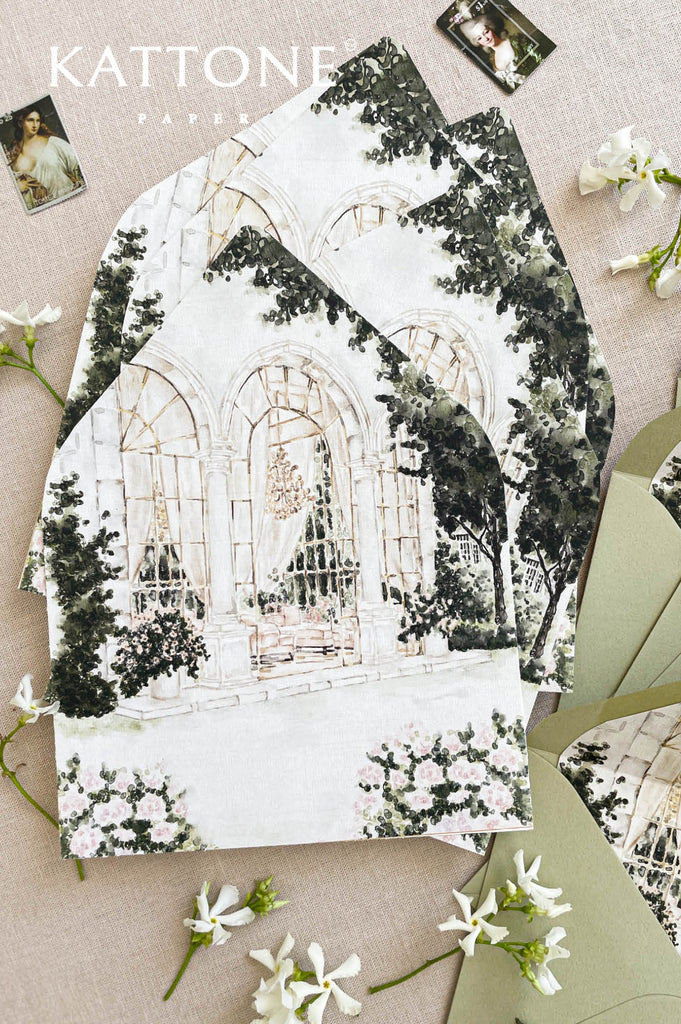 Close-up of watercolor envelope liner showing elegant architectural arches and botanical greenery, printed in fine detail for luxury wedding stationery.