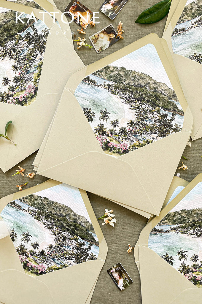 Close-up of watercolor envelope liner showing a tropical coastal landscape with palm trees and ocean, printed on textured paper inside wedding envelopes.