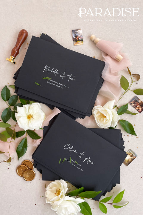 Matte black wedding envelopes with white ink address printing, styled flat lay with florals, wax seal, and greenery, perfect for modern and editorial invitation suites.