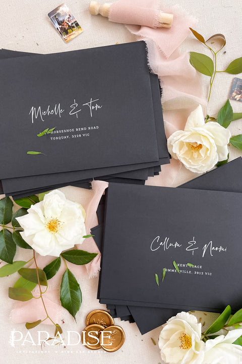 Matte black wedding envelopes with white ink address printing, styled flat lay with florals, wax seal, and greenery, perfect for modern and editorial invitation suites.