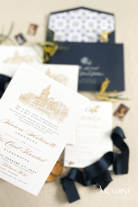 Inspired by the golden light and charm of European summers, this wedding invitation suite combines custom hand-drawn architecture with delicate watercolor lemons for a design that’s both luxurious and full of life. The venue illustration is created by hand, transforming your wedding location into a piece of art that sets the tone for your day. Paired with rich navy envelopes, an ornate blue patterned liner, and velvet ribbon accents, the result is a suite that exudes elegance and personality.