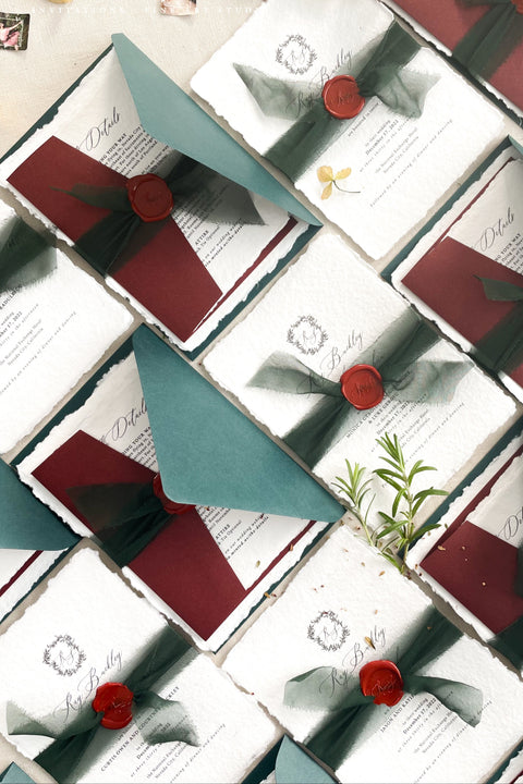 This handmade wedding invitation suite captures the essence of fine art stationery with a touch of deep, moody charm. Printed on luxury cotton paper with natural deckled edges. The suite is adorned with your custom monogram - hand-drawn to reflect your initials and personal style - and wrapped in a forest green silk ribbon with a red wax seal for a dramatic yet refined finish. Paired with rich burgundy backing cards and green envelopes.