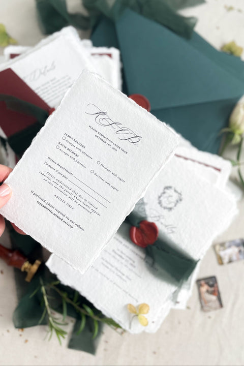 This handmade wedding invitation suite captures the essence of fine art stationery with a touch of deep, moody charm. Printed on luxury cotton paper with natural deckled edges. The suite is adorned with your custom monogram - hand-drawn to reflect your initials and personal style - and wrapped in a forest green silk ribbon with a red wax seal for a dramatic yet refined finish. Paired with rich burgundy backing cards and green envelopes.