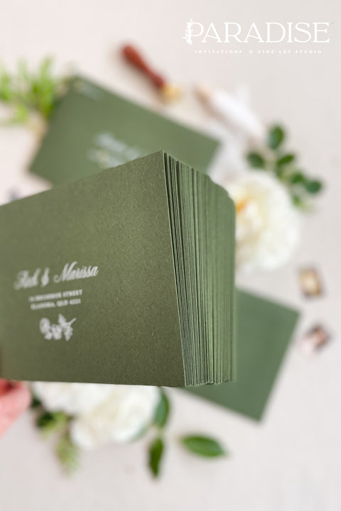 Forest green wedding envelopes with printed addresses, styled flat lay with white florals, wax seals, and greenery, perfect for botanical and elegant invitation suites.