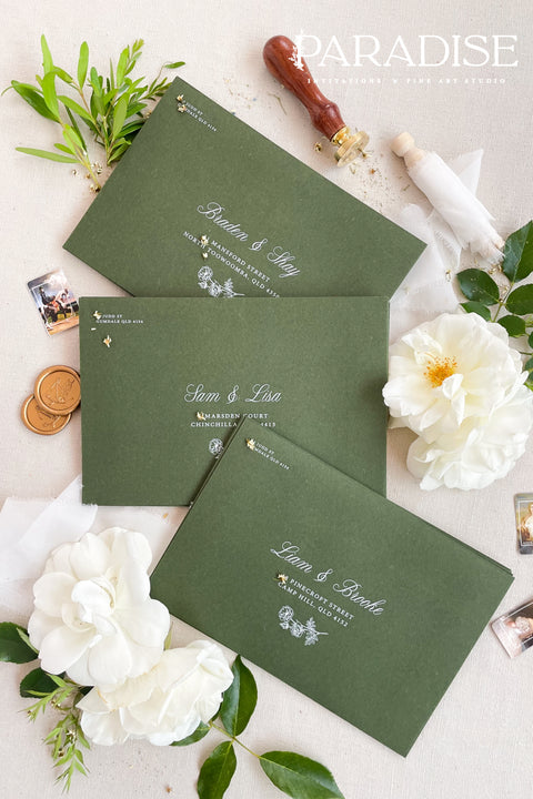 Forest green wedding envelopes with printed addresses, styled flat lay with white florals, wax seals, and greenery, perfect for botanical and elegant invitation suites.